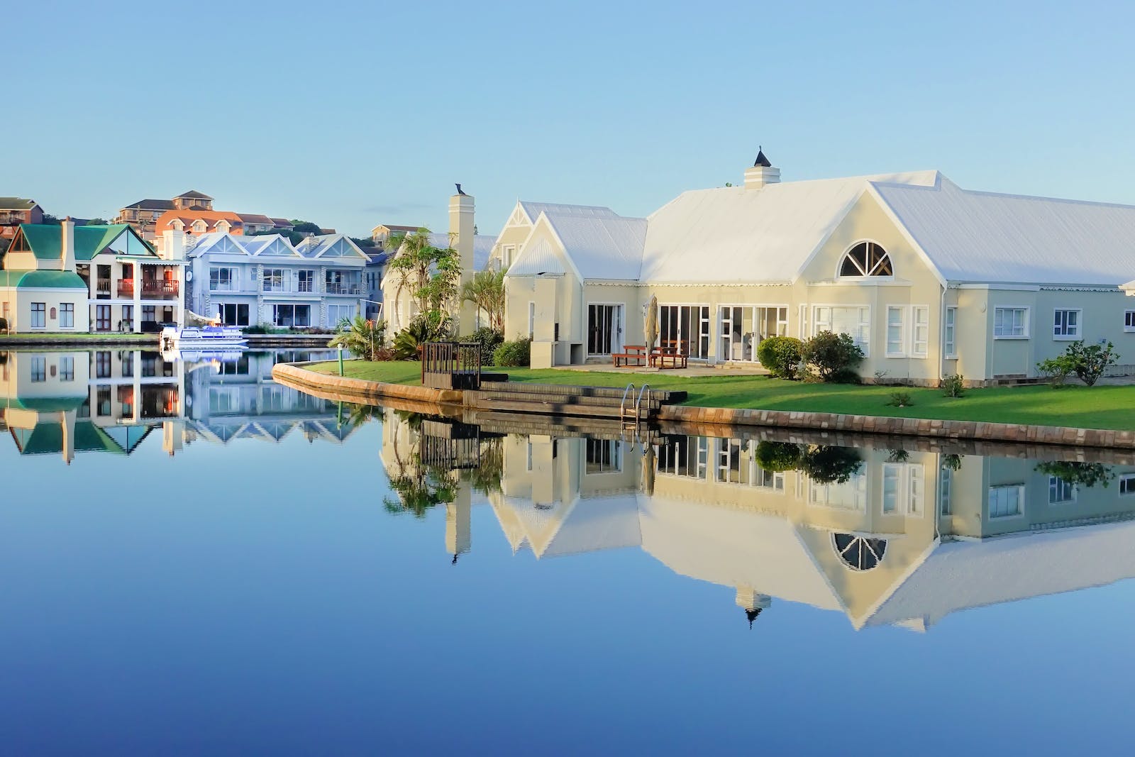 Scenic lakeside homes with clear reflections on calm water, under a blue sky.