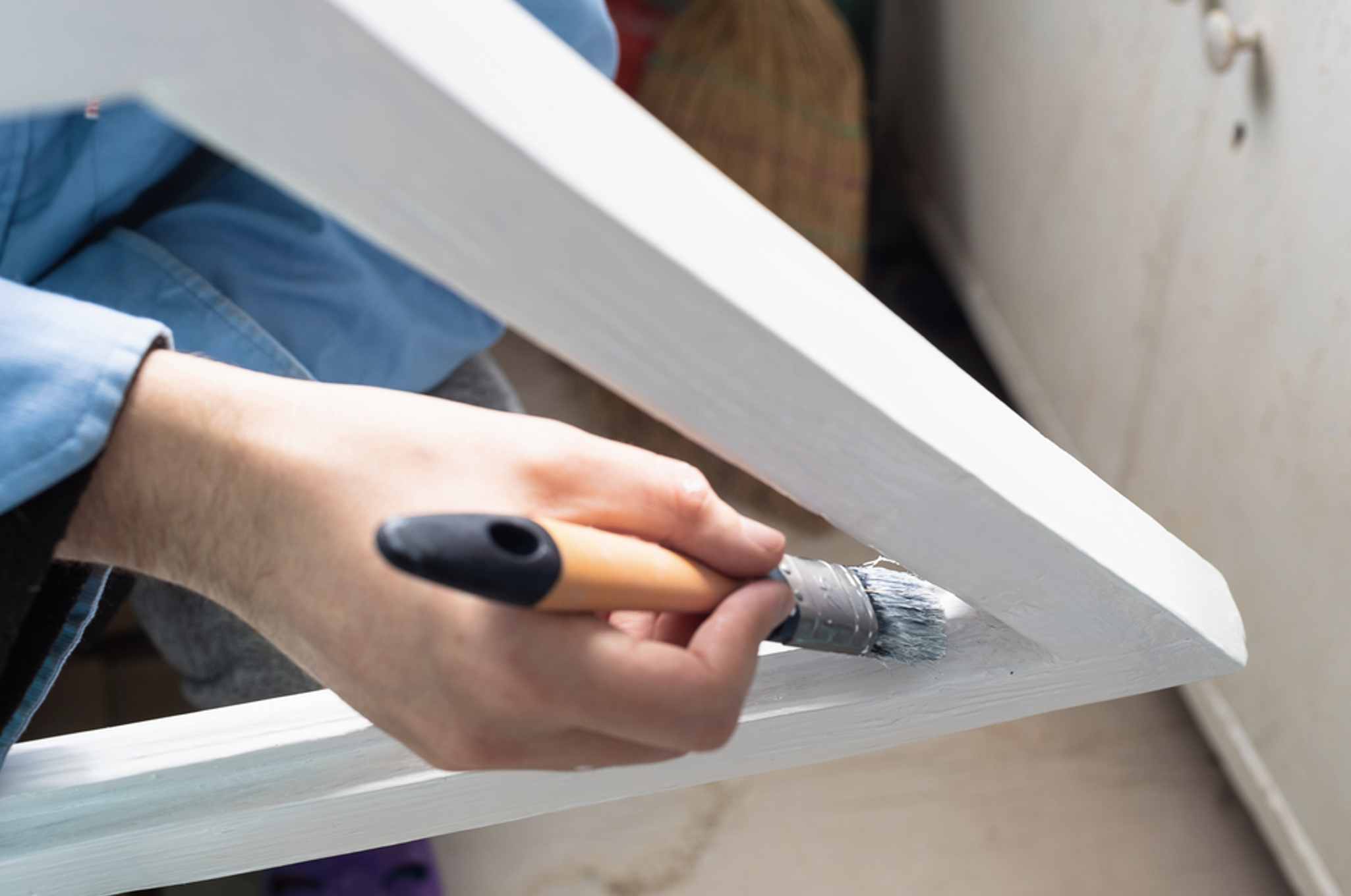 Person painting wooden frame with white paint using a small brush for home improvement project