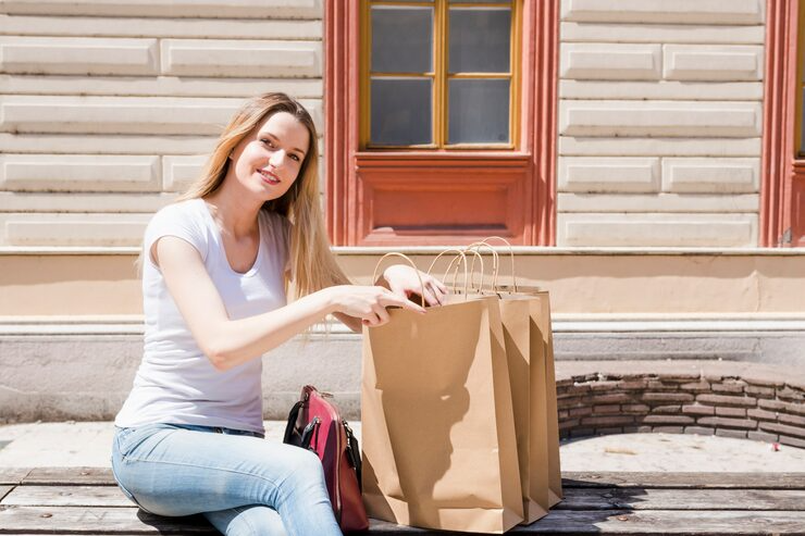A woman sits on a bench, surrounded by shopping bags, appearing relaxed and content in a public space